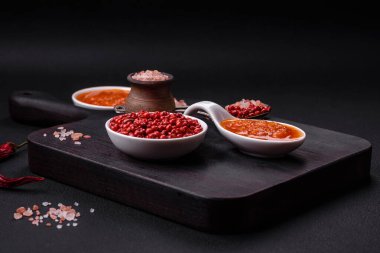 Red adjika sauce or ketchup with spices and herbs on a dark concrete background