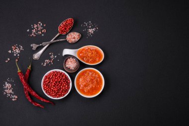 Red adjika sauce or ketchup with spices and herbs on a dark concrete background