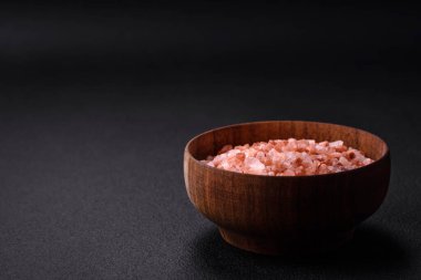 Pink himalayan salt in a wooden bowl on a dark concrete background. Seasonings and additives in the kitchen