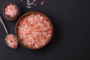 Pink himalayan salt in a wooden bowl on a dark concrete background. Seasonings and additives in the kitchen