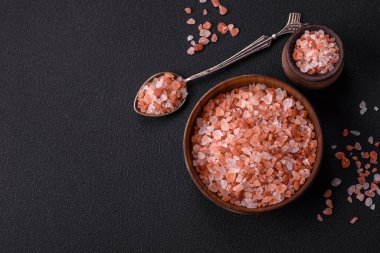 Pink himalayan salt in a wooden bowl on a dark concrete background. Seasonings and additives in the kitchen
