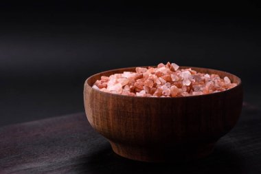Pink himalayan salt in a wooden bowl on a dark concrete background. Seasonings and additives in the kitchen