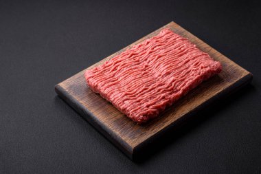Raw beef or pork mince with salt spices and herbs on a wooden cutting board on a dark concrete background