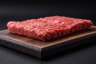 Raw beef or pork mince with salt spices and herbs on a wooden cutting board on a dark concrete background