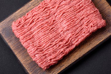 Raw beef or pork mince with salt spices and herbs on a wooden cutting board on a dark concrete background