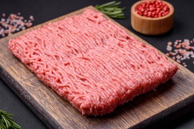 Raw beef or pork mince with salt spices and herbs on a wooden cutting board on a dark concrete background