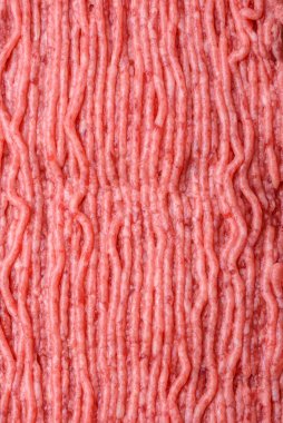 Raw beef or pork mince with salt spices and herbs on a wooden cutting board on a dark concrete background