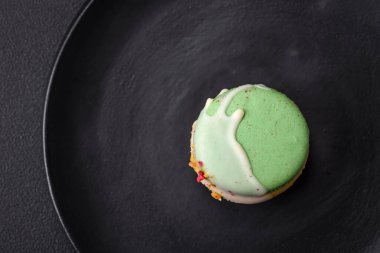 Beautiful tasty macaron with filling and fruit flavor on a black plate on a dark concrete background