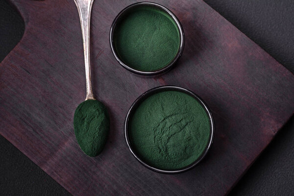 Специя, зеленый цвет спирулина в виде порошка в черной миске на темно-бетонном фоне