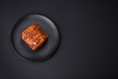 Delicious fresh smoked meat or ham with spices and herbs on a dark concrete background