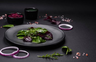 Delicious fresh salad consisting of spinach, chard, radicchio, red chart, bulls blood and arugula on a black plate on a dark concrete background