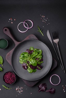 Delicious fresh salad consisting of spinach, chard, radicchio, red chart, bulls blood and arugula on a black plate on a dark concrete background