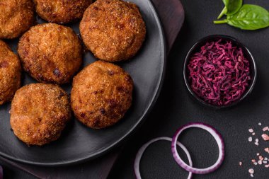 Delicious fresh meat or vegetable cutlets with spices and herbs on a black plate on a dark concrete background