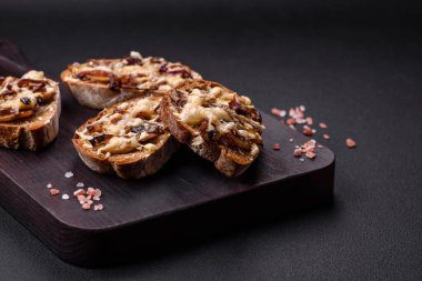 Delicious crispy toast or bruschetta with fried onion, champignon mushrooms and cheese with spices and herbs on a dark concrete background