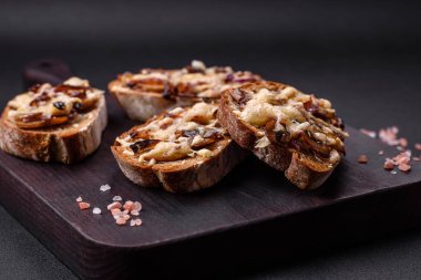 Delicious crispy toast or bruschetta with fried onion, champignon mushrooms and cheese with spices and herbs on a dark concrete background