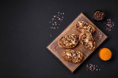 Delicious crispy toast or bruschetta with fried onion, champignon mushrooms and cheese with spices and herbs on a dark concrete background