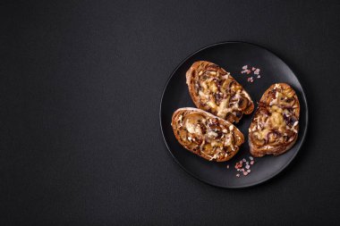 Delicious crispy toast or bruschetta with fried onion, champignon mushrooms and cheese with spices and herbs on a dark concrete background