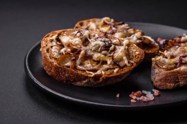Delicious crispy toast or bruschetta with fried onion, champignon mushrooms and cheese with spices and herbs on a dark concrete background