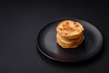 Delicious fresh pancakes with berry jam on a black ceramic plate on a dark concrete background