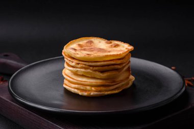 Delicious fresh pancakes with berry jam on a black ceramic plate on a dark concrete background