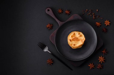 Delicious fresh pancakes with berry jam on a black ceramic plate on a dark concrete background