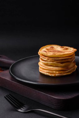 Delicious fresh pancakes with berry jam on a black ceramic plate on a dark concrete background