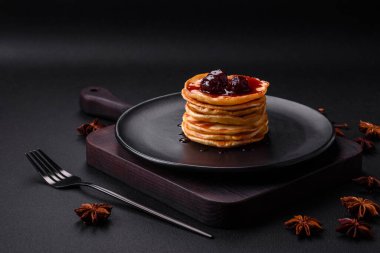Delicious fresh pancakes with berry jam on a black ceramic plate on a dark concrete background
