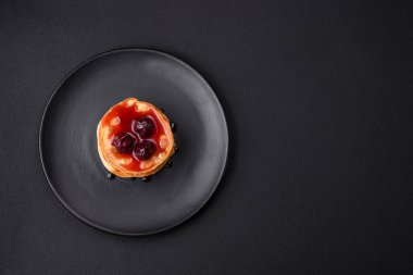 Delicious fresh pancakes with berry jam on a black ceramic plate on a dark concrete background