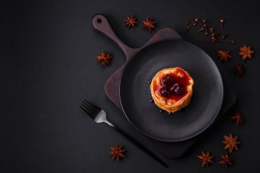Delicious fresh pancakes with berry jam on a black ceramic plate on a dark concrete background