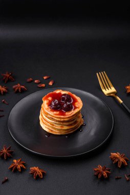 Delicious fresh pancakes with berry jam on a black ceramic plate on a dark concrete background