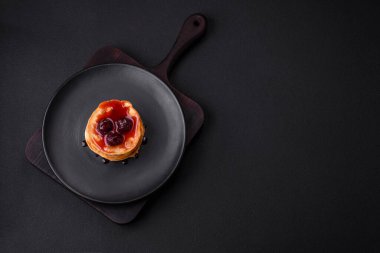 Delicious fresh pancakes with berry jam on a black ceramic plate on a dark concrete background