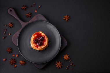 Delicious fresh pancakes with berry jam on a black ceramic plate on a dark concrete background