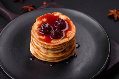 Delicious fresh pancakes with berry jam on a black ceramic plate on a dark concrete background