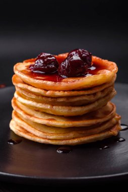 Delicious fresh pancakes with berry jam on a black ceramic plate on a dark concrete background