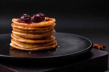 Delicious fresh pancakes with berry jam on a black ceramic plate on a dark concrete background
