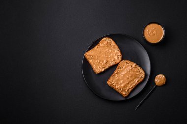 Nutritious sandwich consisting of bread and peanut butter on a black ceramic plate on a dark concrete background