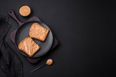 Nutritious sandwich consisting of bread and peanut butter on a black ceramic plate on a dark concrete background