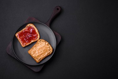 Nutritious sandwiches consisting of bread, raspberry jam and peanut butter on a black ceramic plate on a dark concrete background