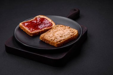 Nutritious sandwiches consisting of bread, raspberry jam and peanut butter on a black ceramic plate on a dark concrete background