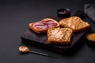 Nutritious sandwiches consisting of bread, raspberry jam and peanut butter on a black ceramic plate on a dark concrete background