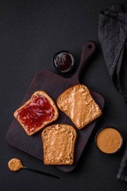 Nutritious sandwiches consisting of bread, raspberry jam and peanut butter on a black ceramic plate on a dark concrete background