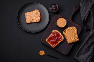 Nutritious sandwiches consisting of bread, raspberry jam and peanut butter on a black ceramic plate on a dark concrete background
