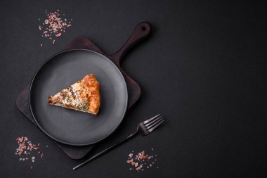Delicious quiche with chicken, cheese, herbs, spices and herbs on a dark concrete background