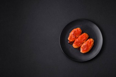 Meat cutlet or meatballs in tomato sauce with garlic, salt, spices and herbs on a black plate on a dark concrete background