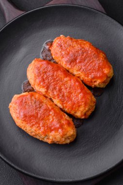 Meat cutlet or meatballs in tomato sauce with garlic, salt, spices and herbs on a black plate on a dark concrete background