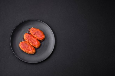 Meat cutlet or meatballs in tomato sauce with garlic, salt, spices and herbs on a black plate on a dark concrete background