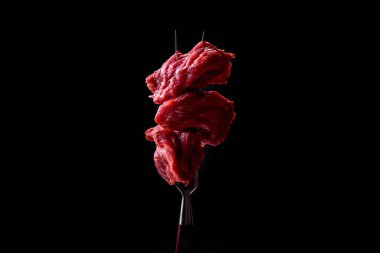 Raw beef cut into several pieces on a wooden cutting board on a dark concrete background