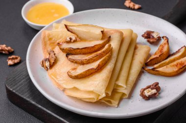 Delicious fresh baked pancakes with honey and fruits on a textured concrete background. Useful healthy food