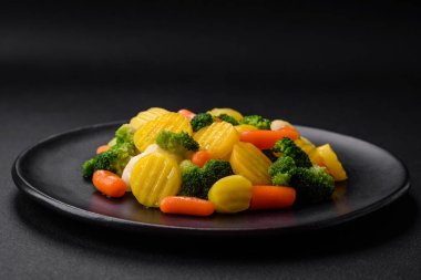 Delicious fresh vegetables steamed carrots, broccoli, cauliflower on a black plate on a dark concrete background
