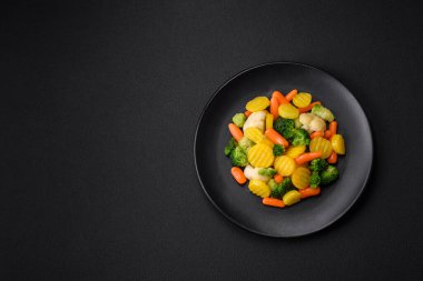 Delicious fresh vegetables steamed carrots, broccoli, cauliflower on a black plate on a dark concrete background